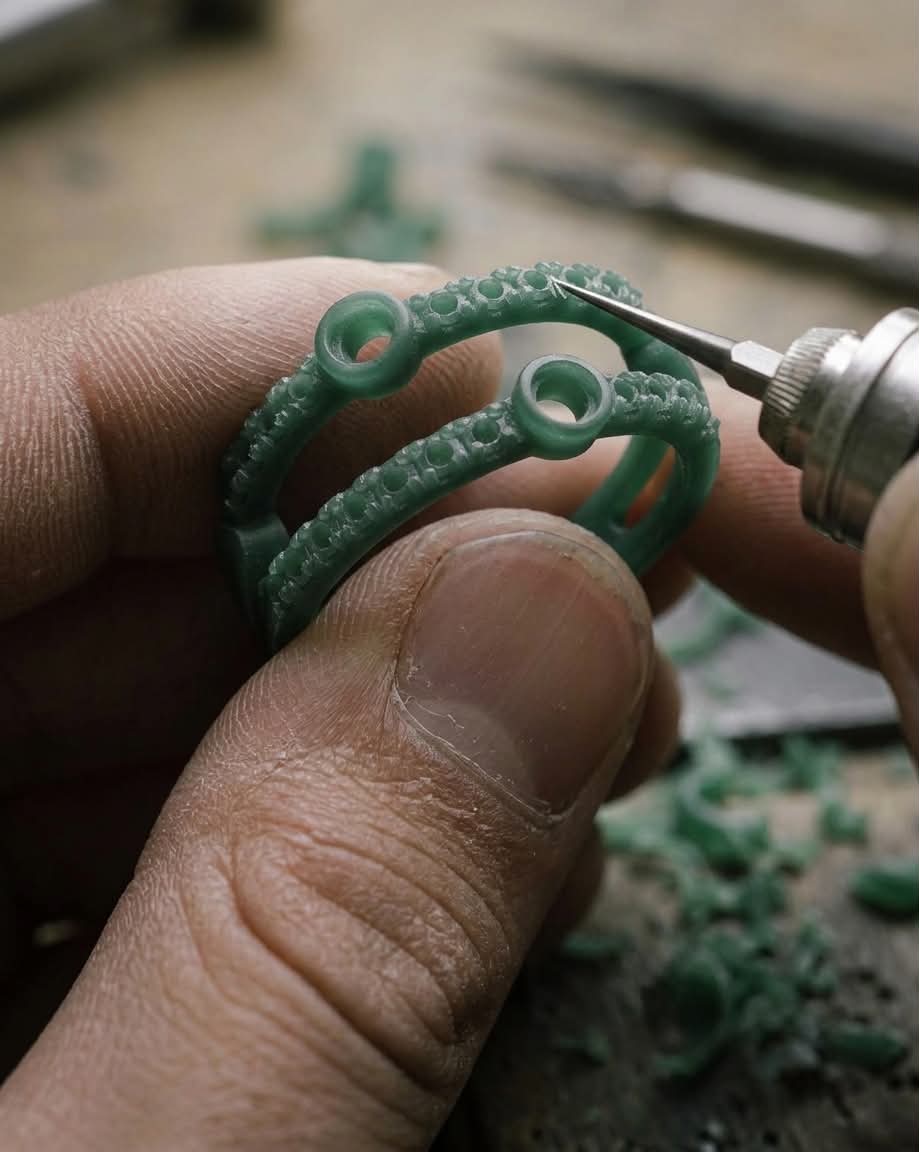 A green wax ring model being carved by hand with a fine engraving tool