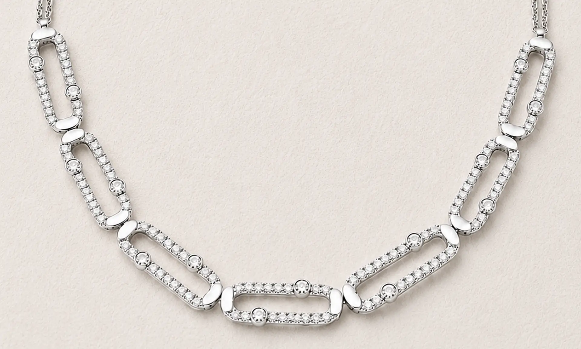 Diamond-set white gold link necklace laid on a warm sand ground