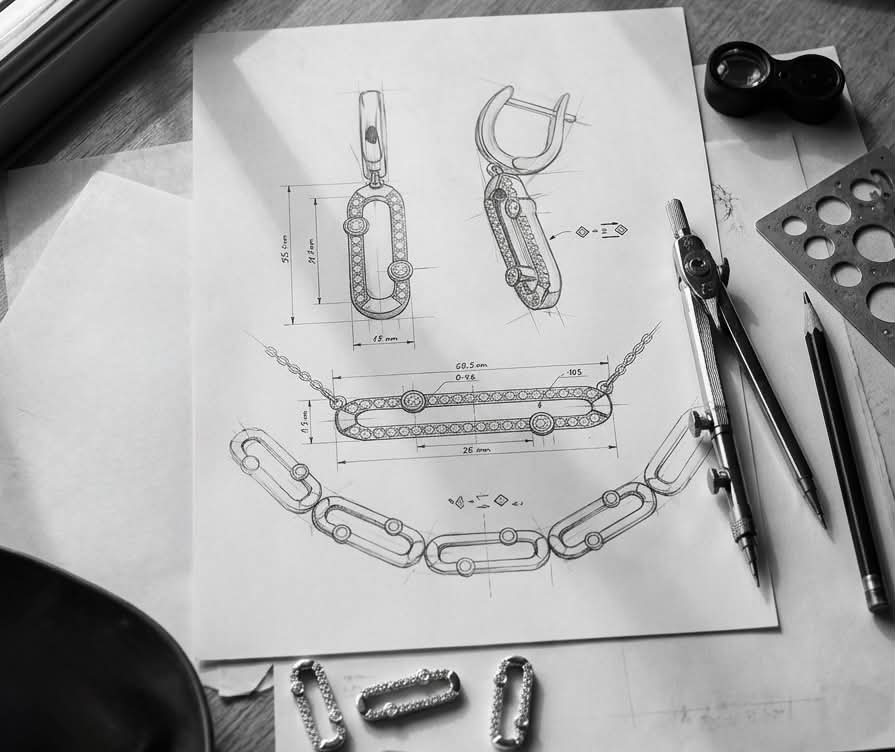 Hand-drawn jewellery design sketches with dividers, pencils and a loupe on a workbench